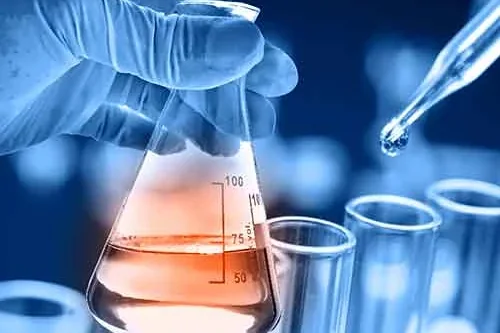 A gloved hand drawing liquid from a flask with a pipette